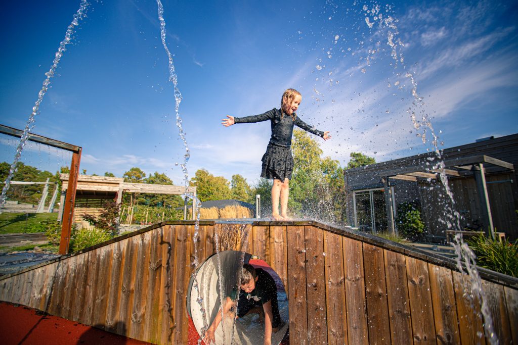 Jente og gutt leker med vann utendørs på Stine Sofie Senteret